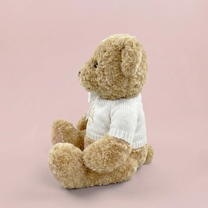 A traditional style seated teddy bear with a white knitted jumper embroidered with a crown or tiara design and the year 2026 in gold thread.