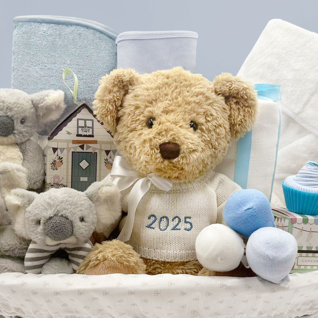 Teddy bear wearing a knitted jumper with '2025' on it, surrounded by baby gifts